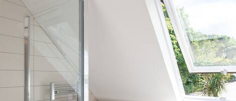 Un baño moderno con cabina de ducha de vidrio, inodoro blanco y tragaluz.
