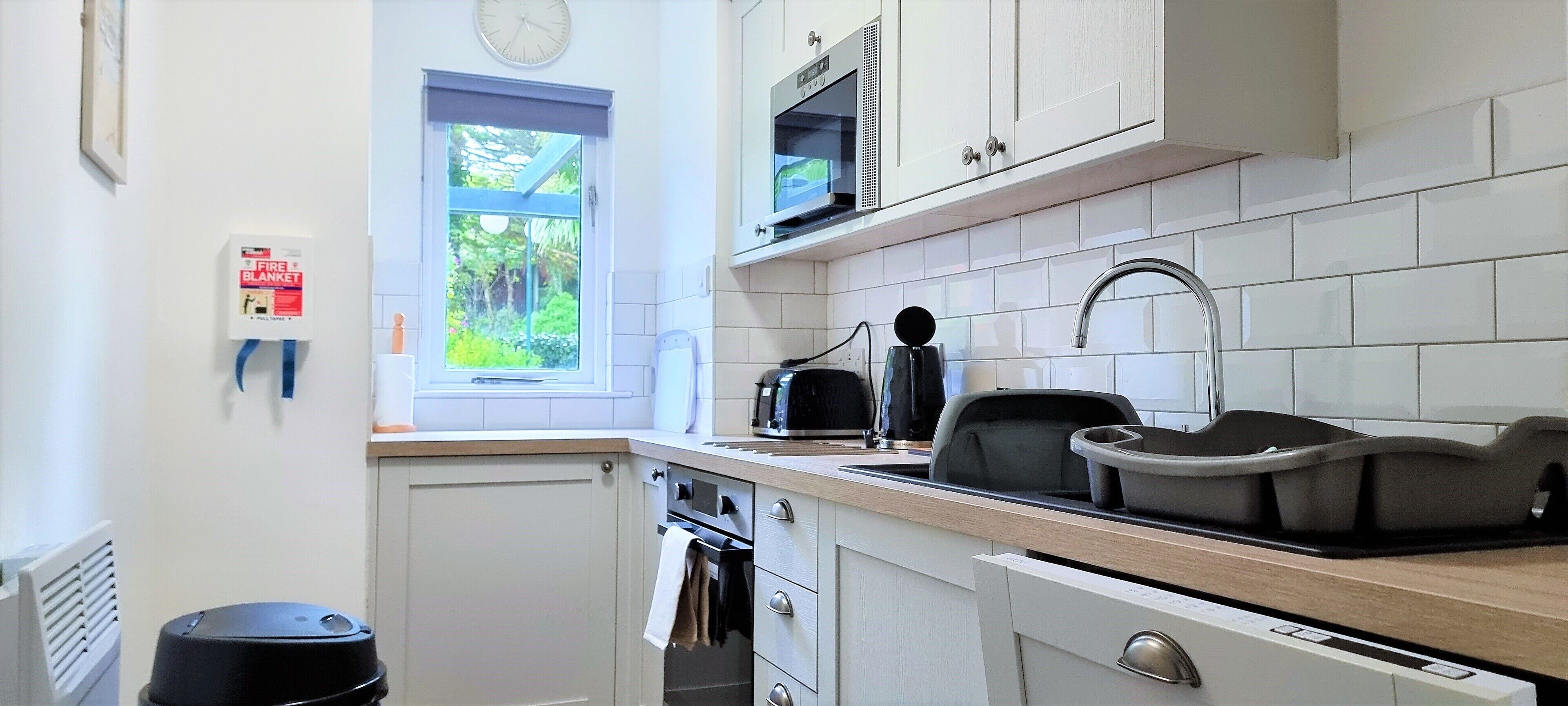A modern kitchen with white cabinets, a built-in oven, a microwave, and a sink.