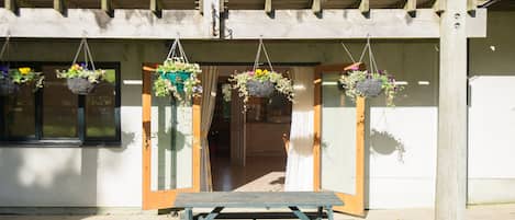 A wooden balcony with hanging flower baskets, a wooden bench, and a potted plant on the ground.