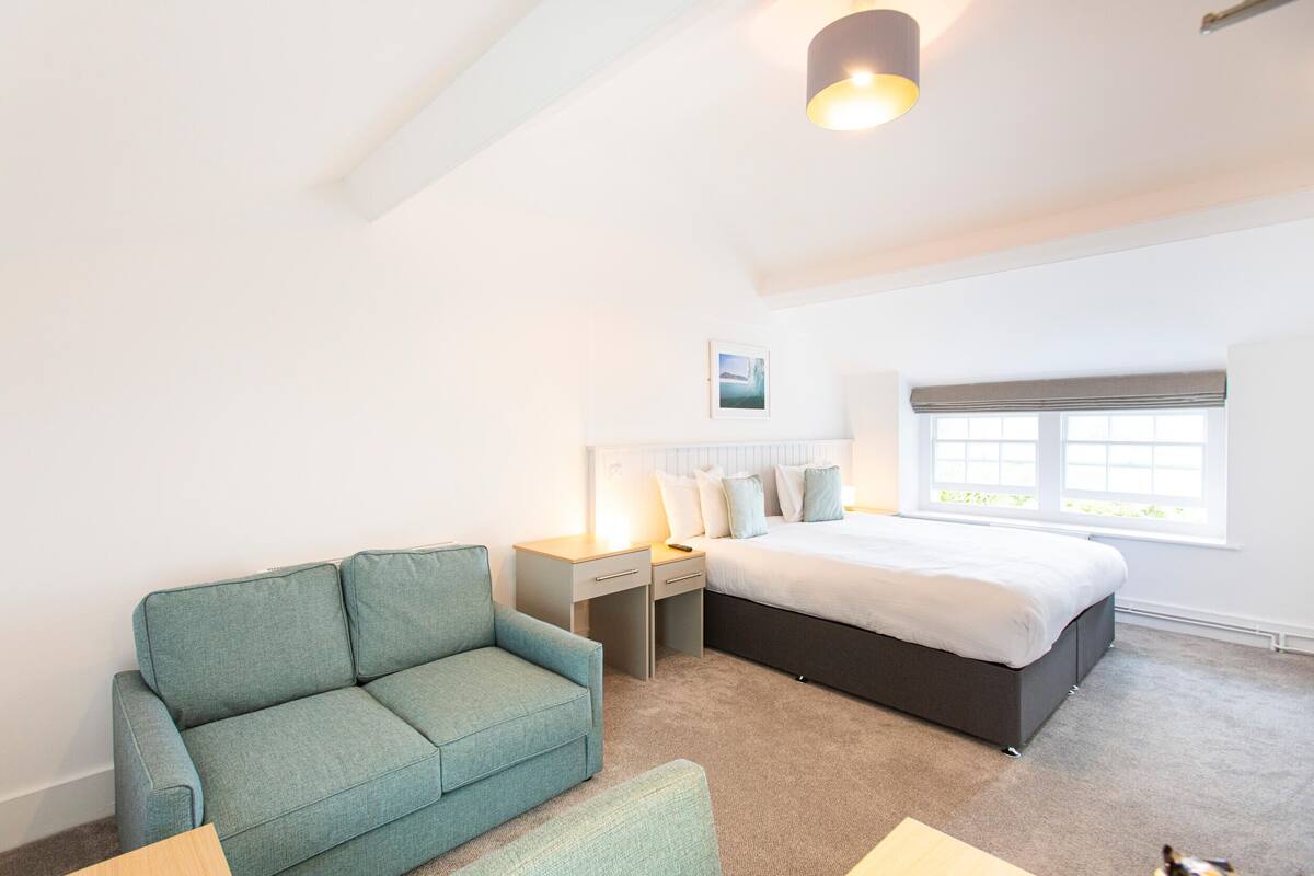 A bedroom with a bed, a sofa, a desk, and a window.