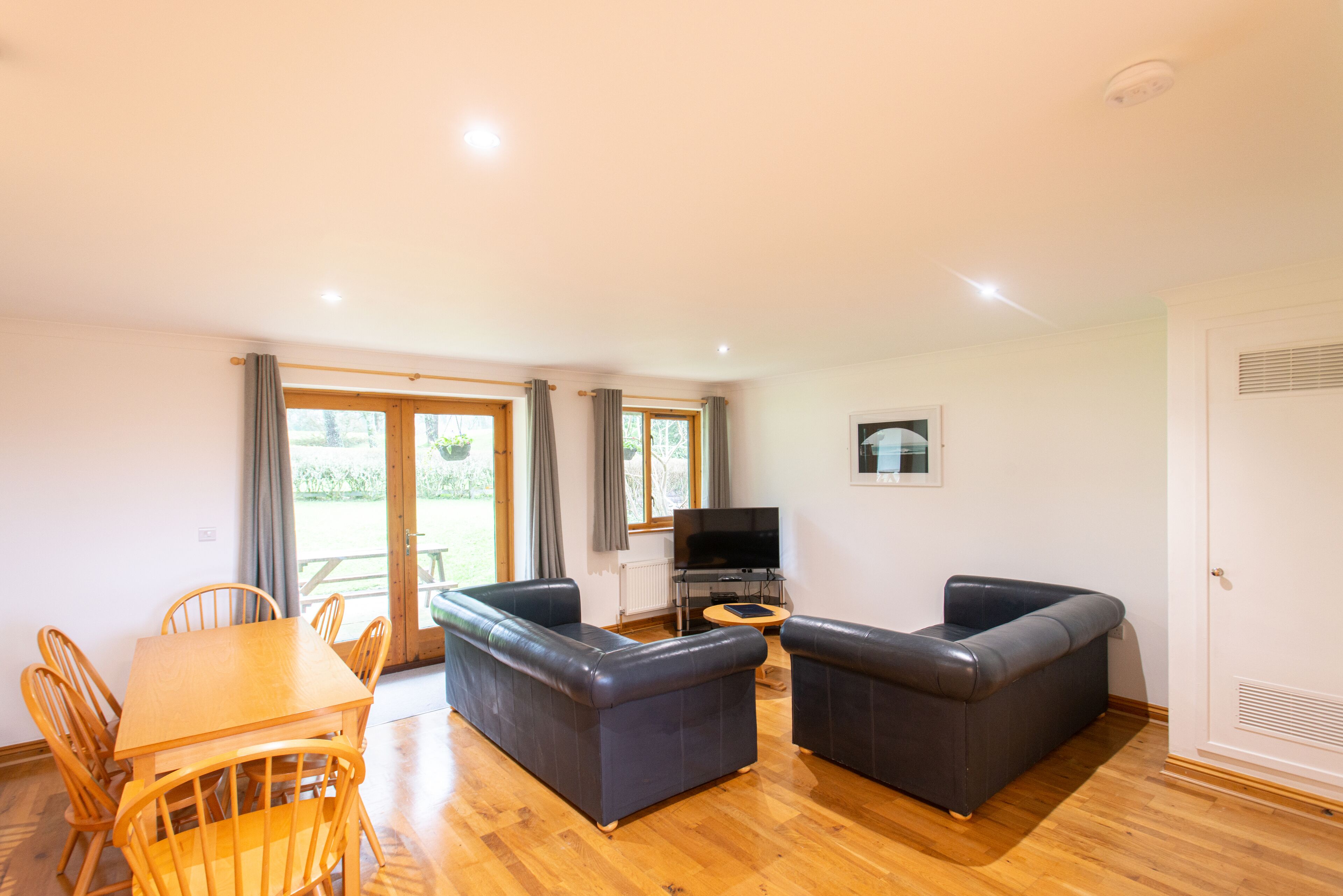 A living room with a wooden table, two sofas, a TV, and a sliding glass door to the outside.