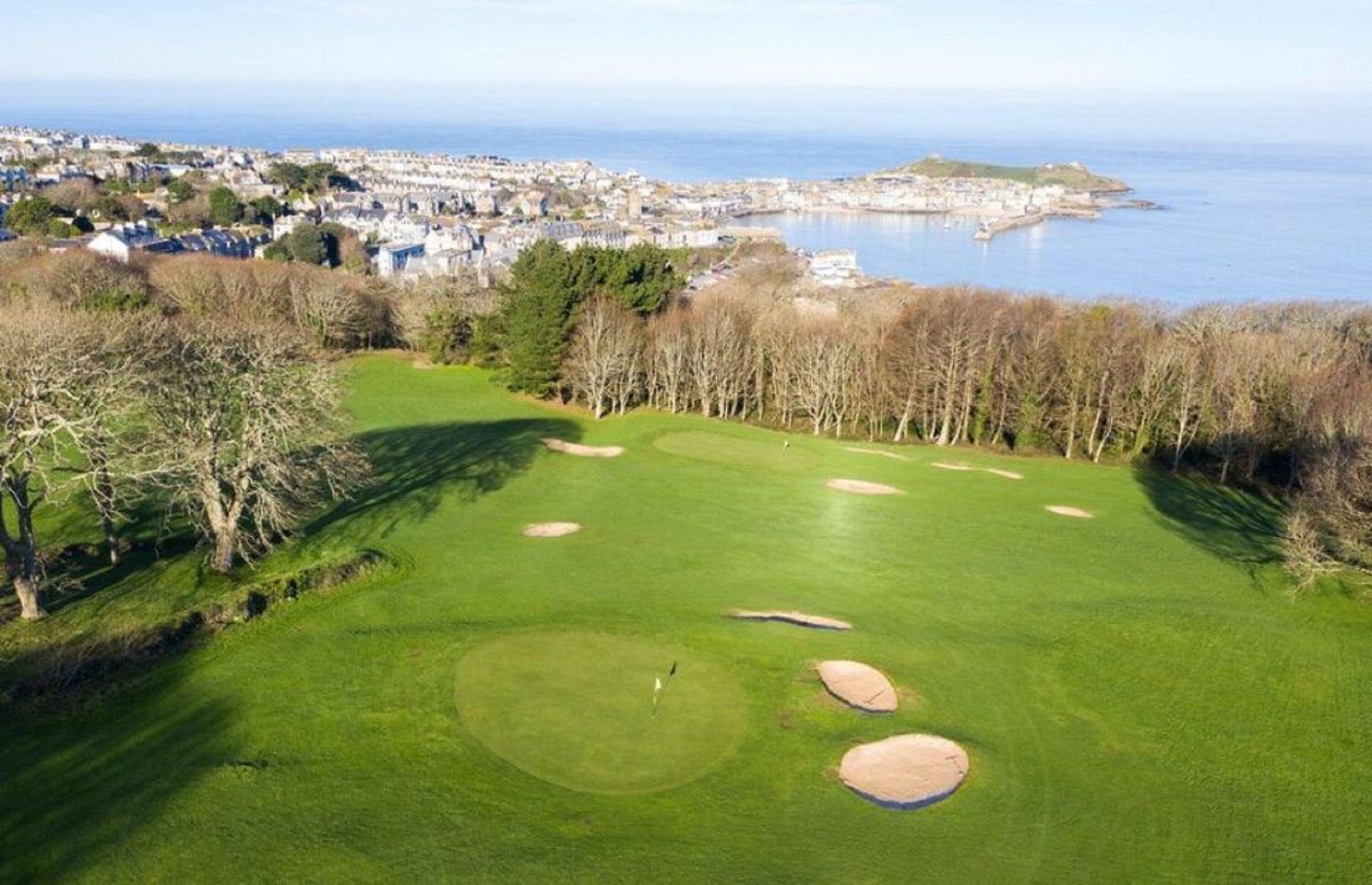 A golf course with bunkers and a view of a coastal town.