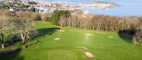 A golf course with bunkers and a view of a coastal town.