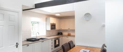 Una cocina compacta con armarios blancos, una mesa de comedor de madera y un reloj en la pared.