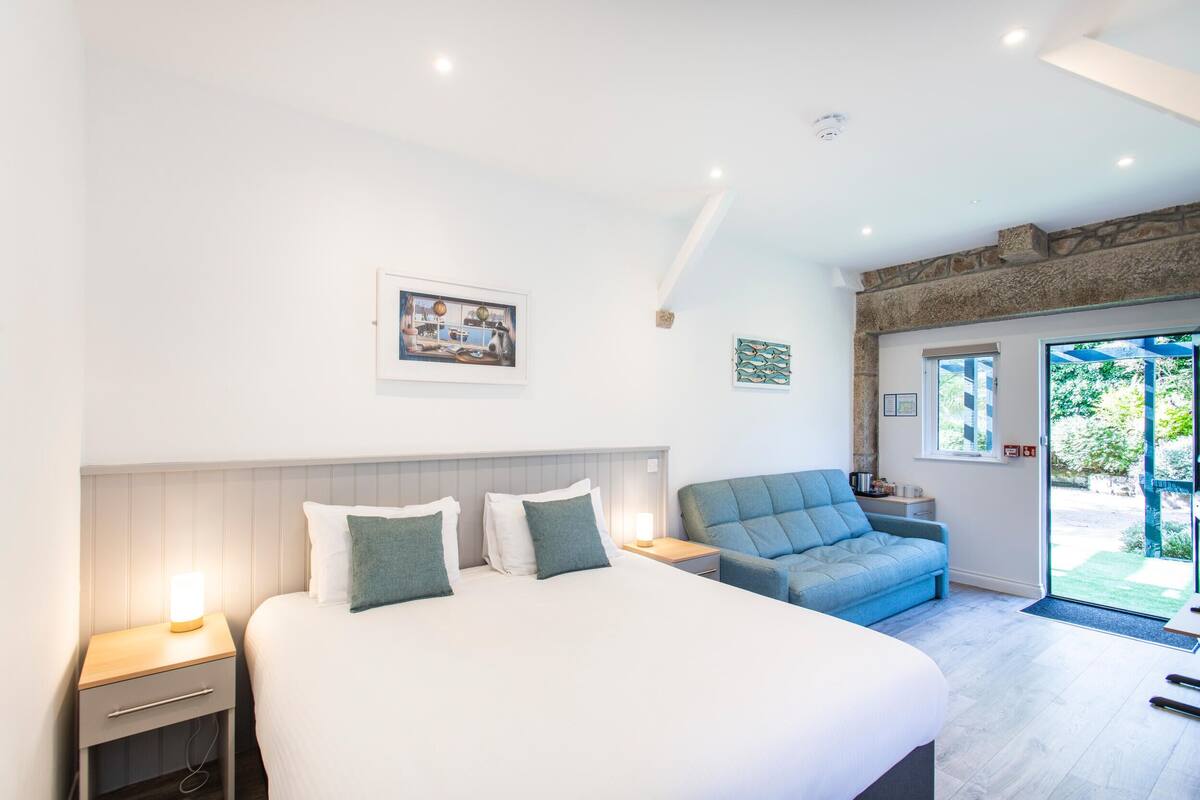 A modern bedroom with a large bed, a nightstand, a blue sofa, and a view of the outdoors.