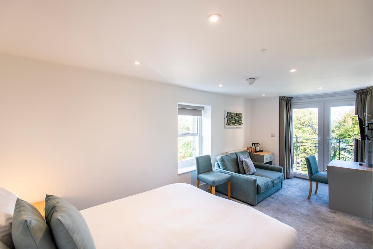 A modern hotel room with a large bed, a sofa, a desk, and a balcony with a view.