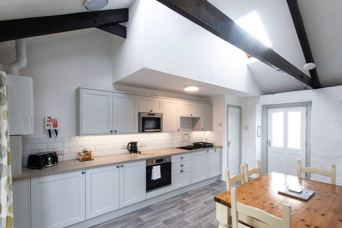 A modern kitchen with white cabinets, a wooden countertop, a built-in oven, and a dining area with a wooden table and chairs.
