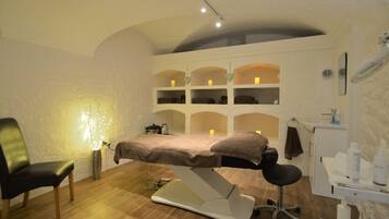 Relax in this serene space with a massage table at its center, surrounded by a chair, candles, and a mirror.