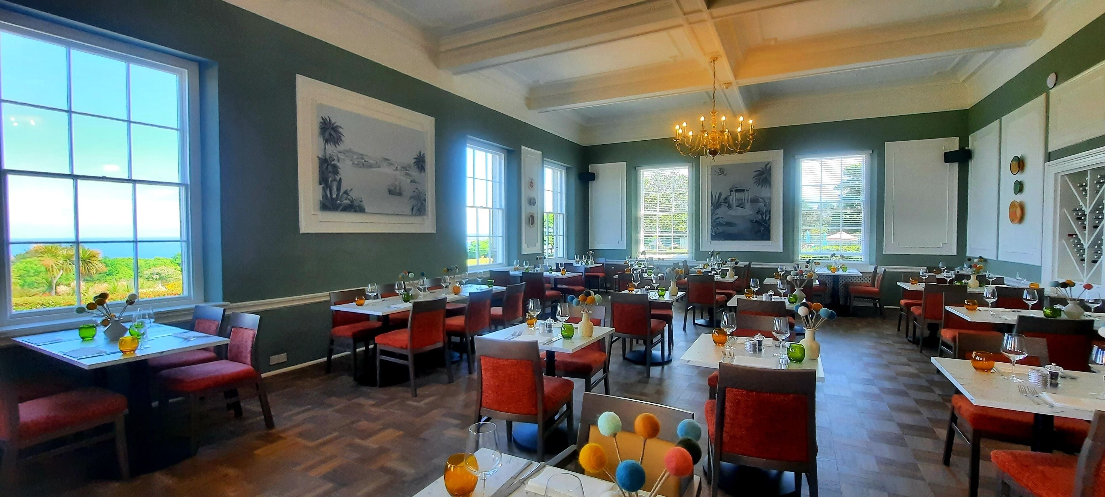 A restaurant with multiple tables and chairs, large windows, and artwork on the walls.