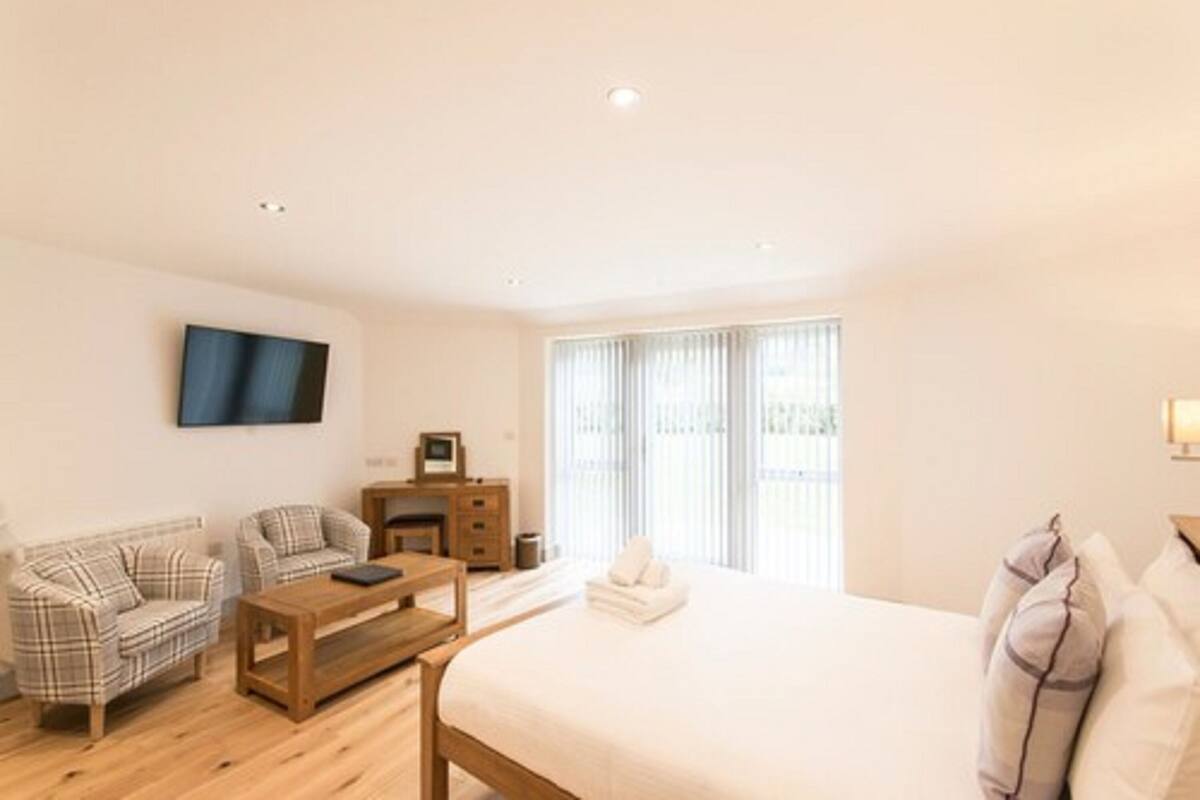 A hotel room with a bed, two sofas, a wooden coffee table, a TV, a dresser, and a window with curtains.