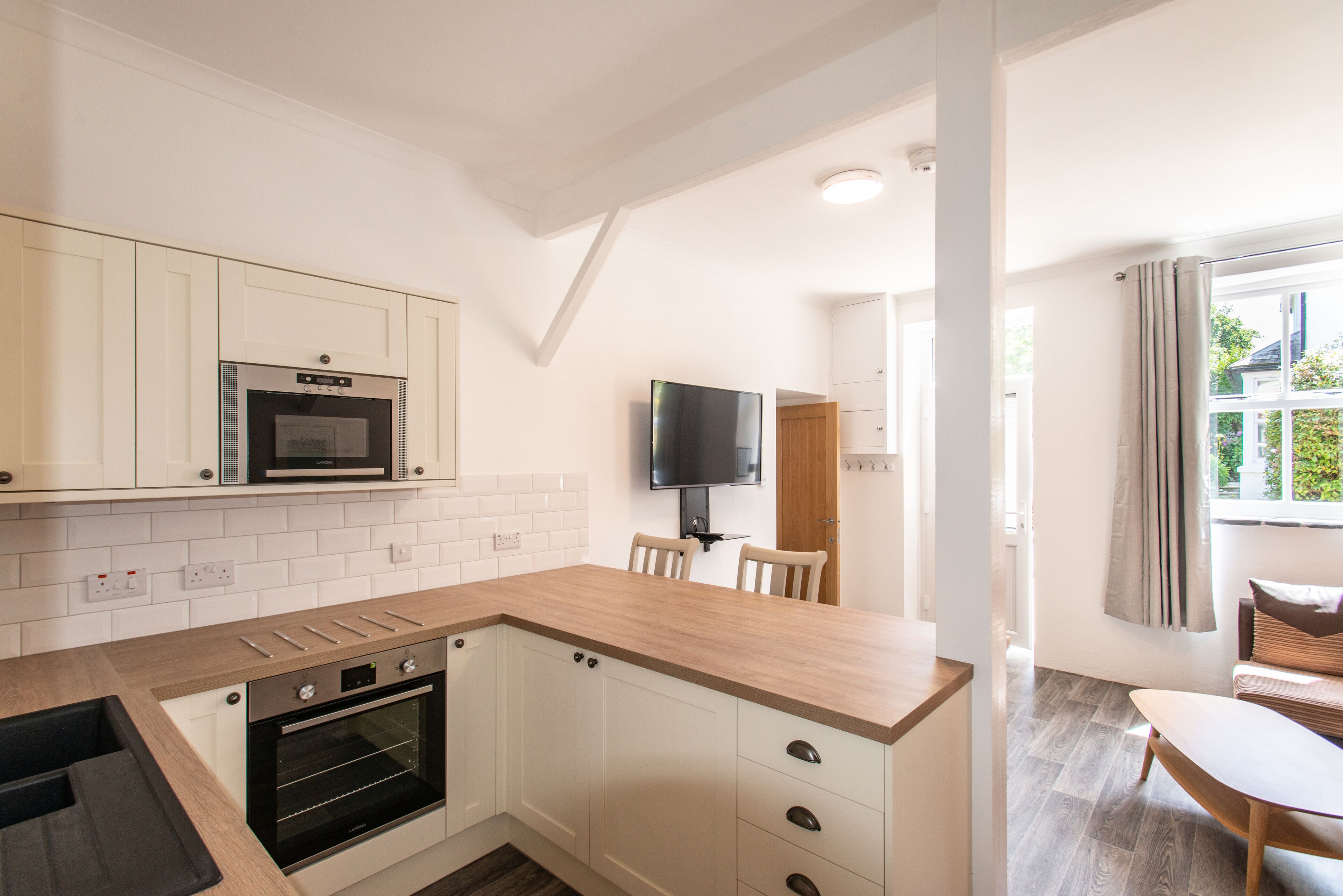 A modern kitchen with white cabinets, a microwave, an oven, and a wooden countertop.