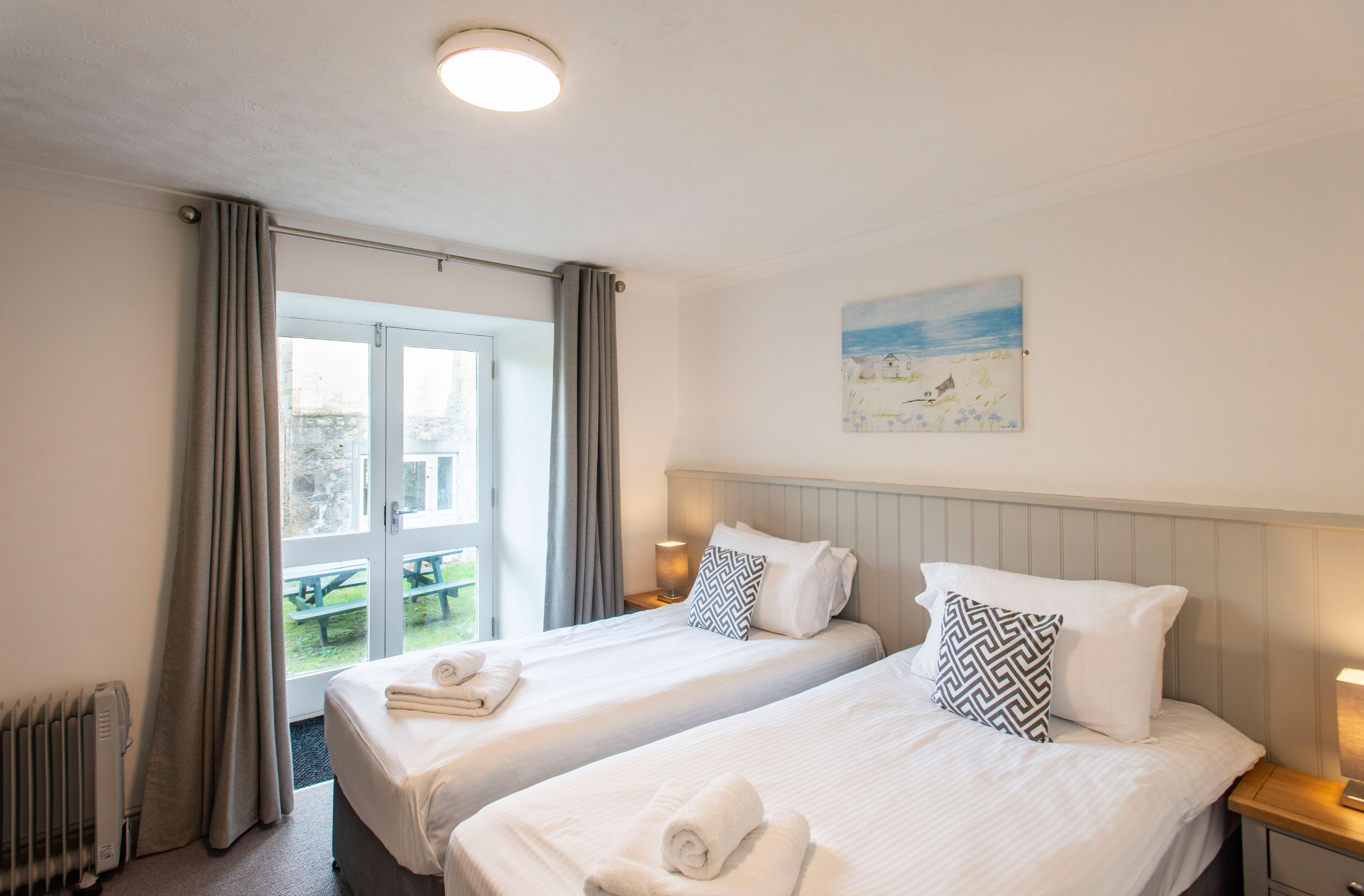 Camera d'albergo con due letti, un quadro appeso al muro e vista su uno spazio esterno.