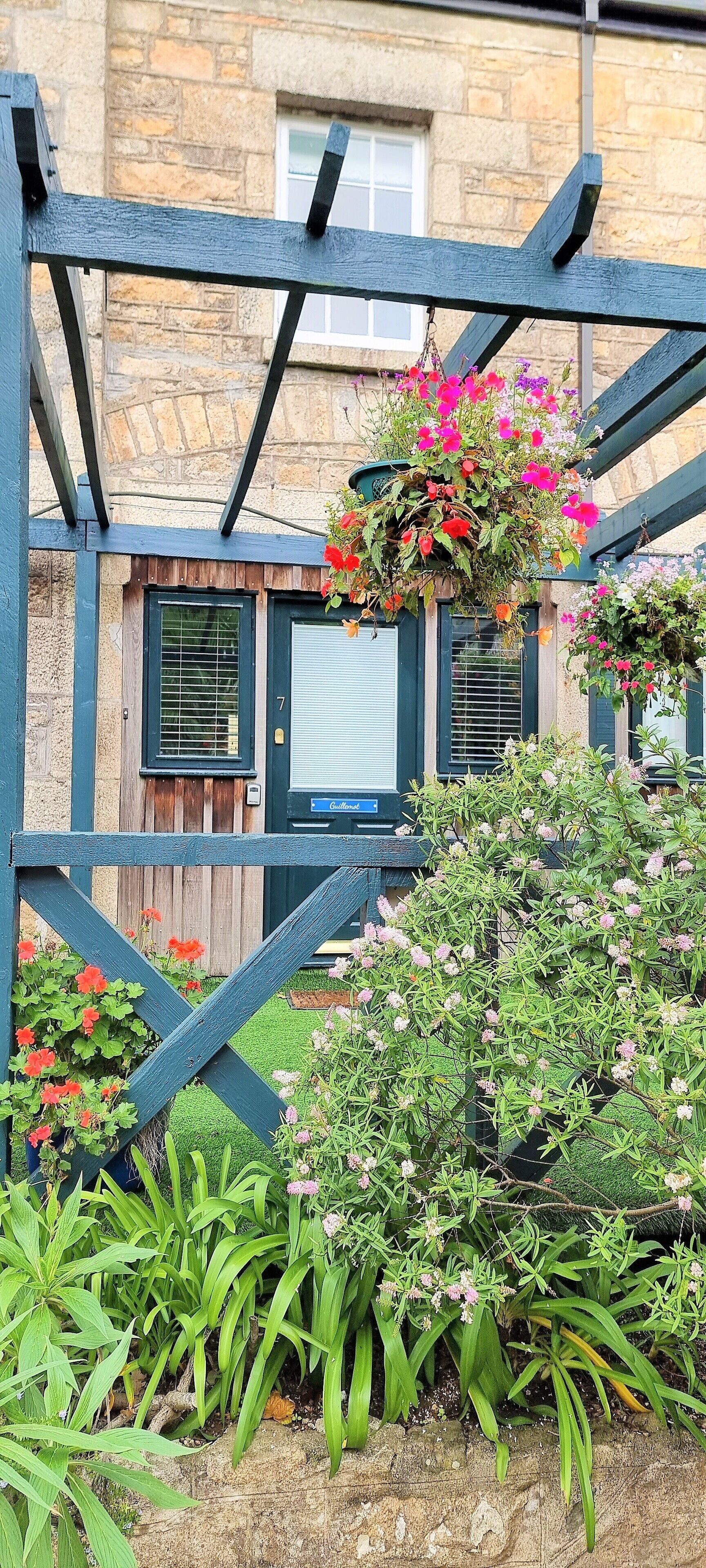 Una pérgola de madera con macetas colgantes de flores y diversas plantas.