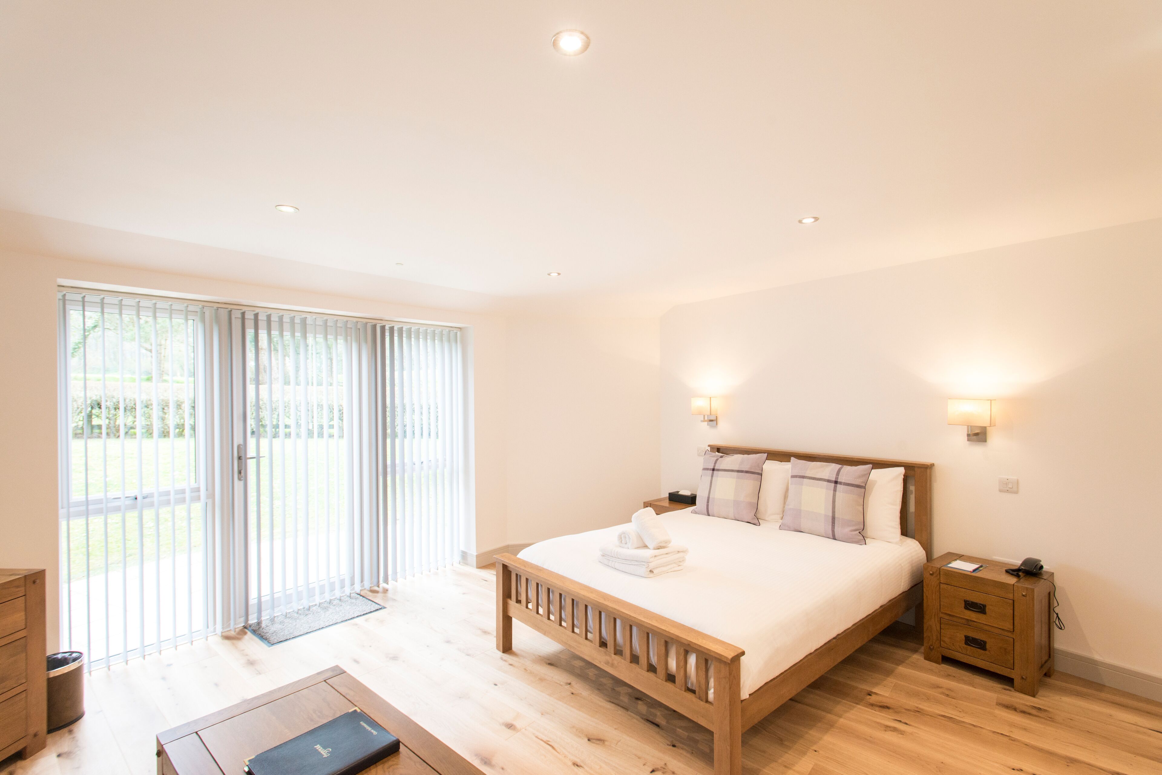 A bedroom with a wooden bed, bedside tables, a nightstand, and a sliding glass door leading to an outdoor area.