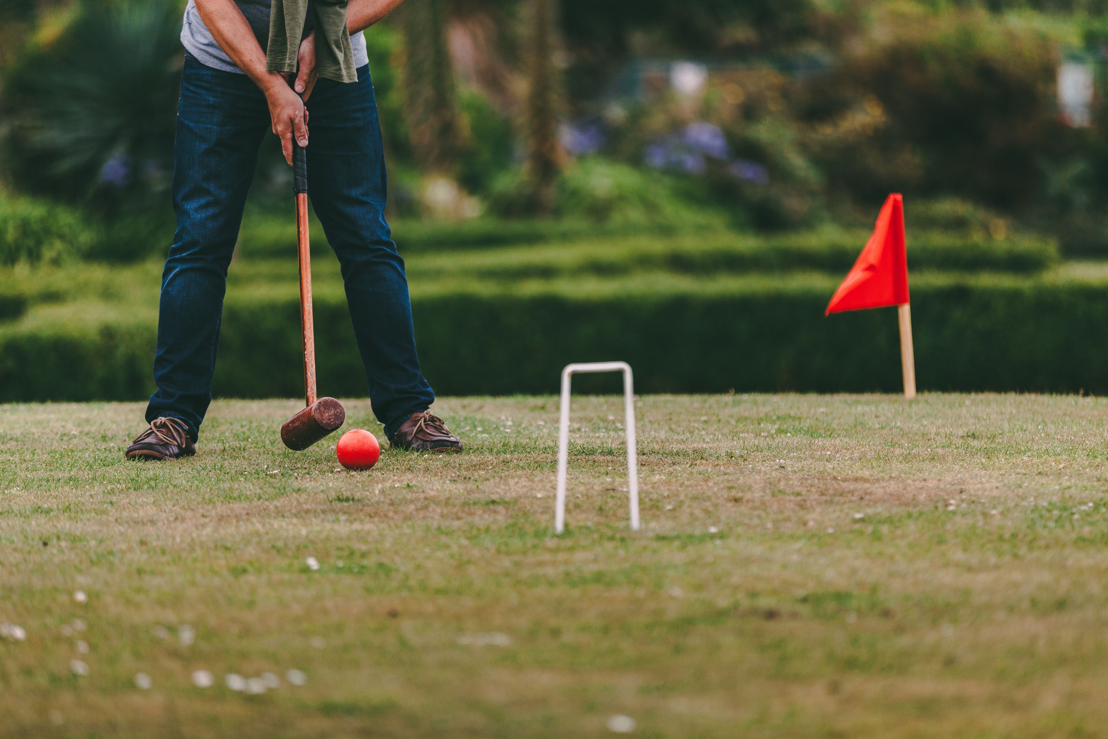 A person playing croquet with a red ball and a white wicket on a grassy field.
