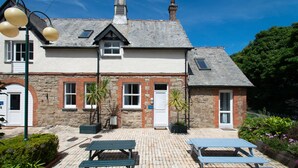 Un bâtiment en pierre doté d’une terrasse carrelée, de deux bancs et d’un petit espace jardin.