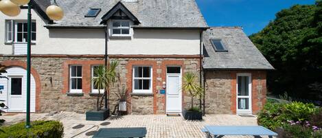 A stone building with a tiled patio, two benches, and a small garden area.