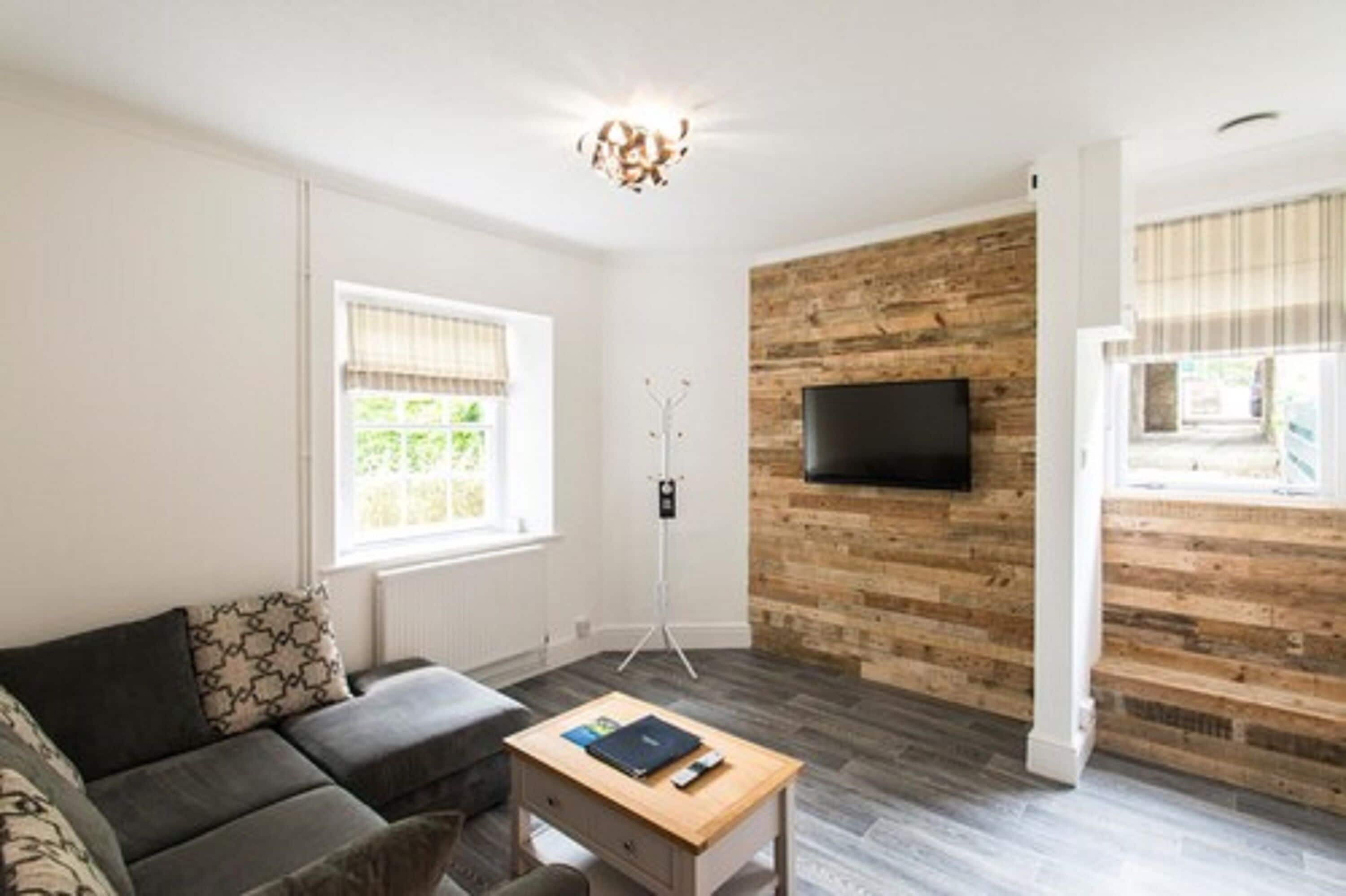 A modern living room with a grey sofa, a wooden coffee table, a mounted TV, and a wooden accent wall.
