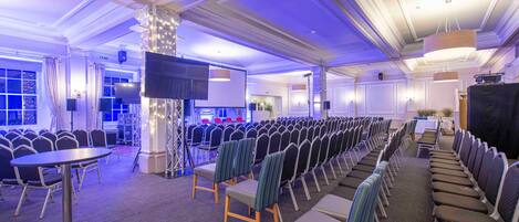 A conference room with rows of chairs, a stage with a screen, and a large pillar with lights.