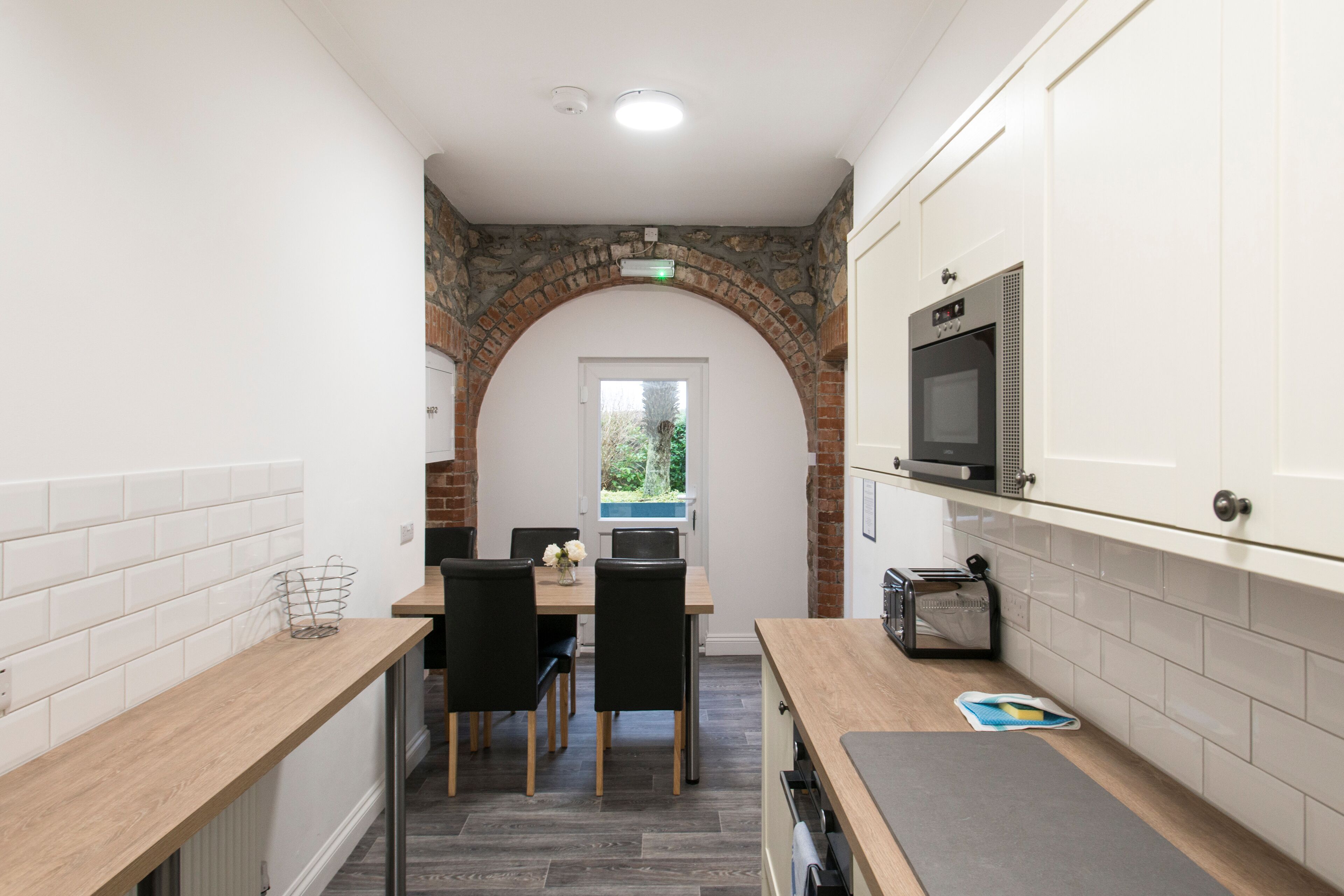 A modern kitchen with white cabinets, a brick archway, a dining area with a table and chairs, and a microwave above the counter.