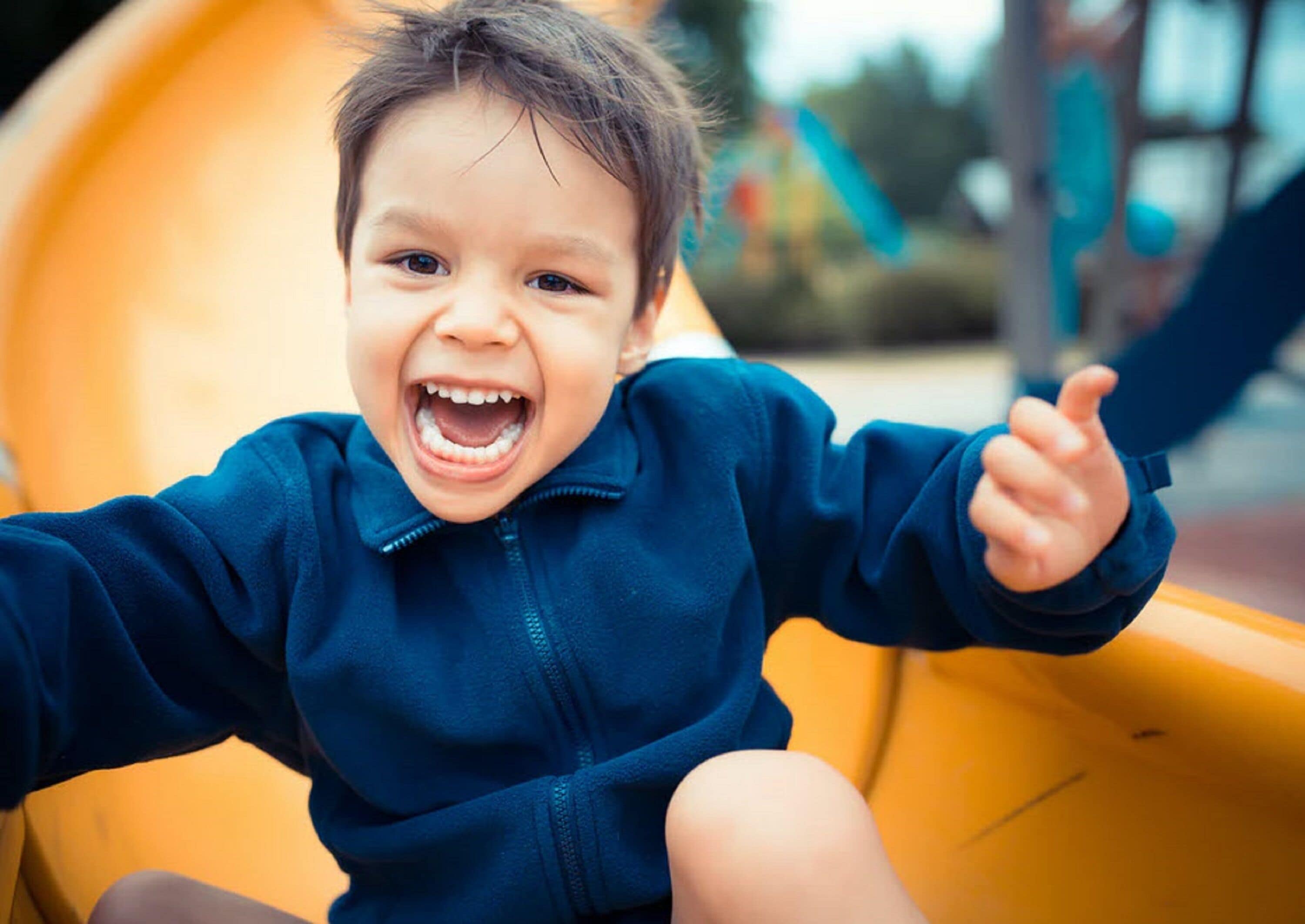 A child sitting on a yellow slide at a playground.