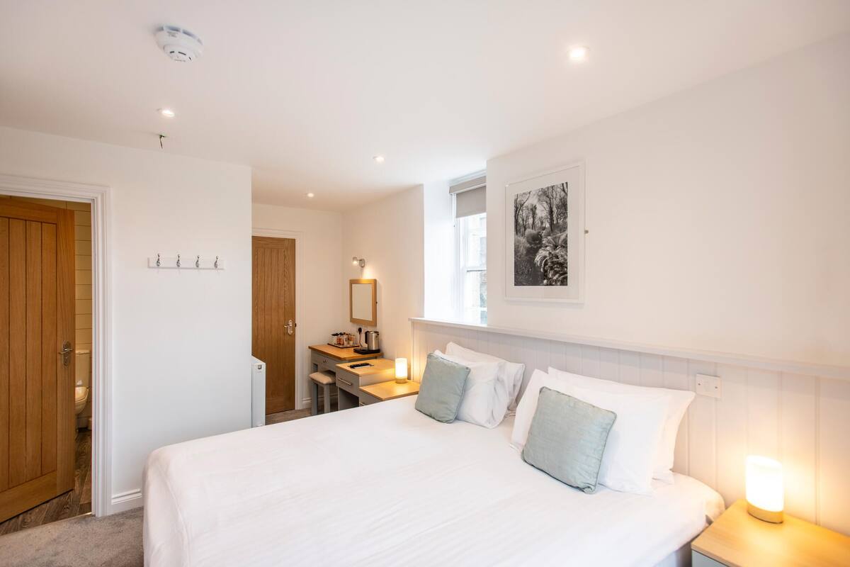 A hotel room with a large bed, a desk with a chair, a small bathroom, and a framed picture on the wall.