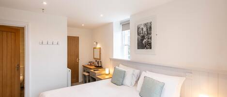 A hotel room with a large bed, a desk with a chair, a small bathroom, and a framed picture on the wall.