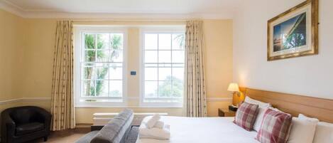A hotel room with a large bed, a sofa, a chair, a lamp, and a painting on the wall.