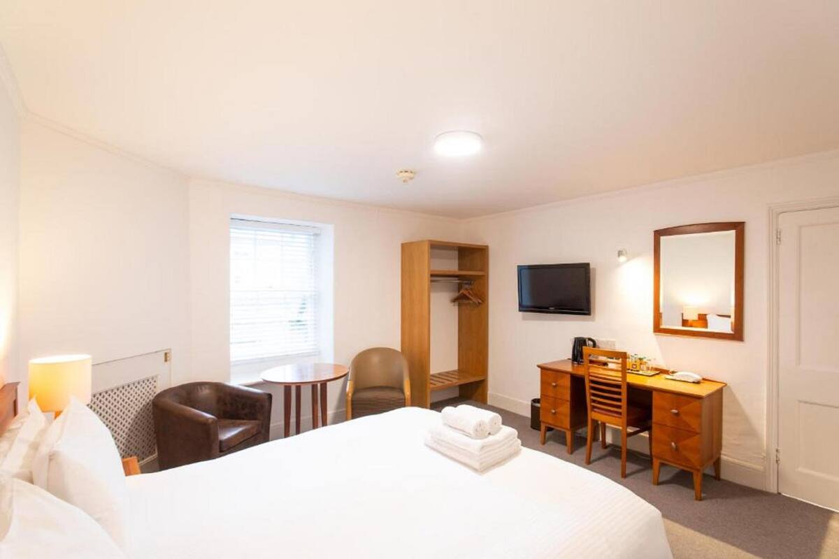 A hotel room with a bed, a desk, a chair, a TV, a wardrobe, and a window.