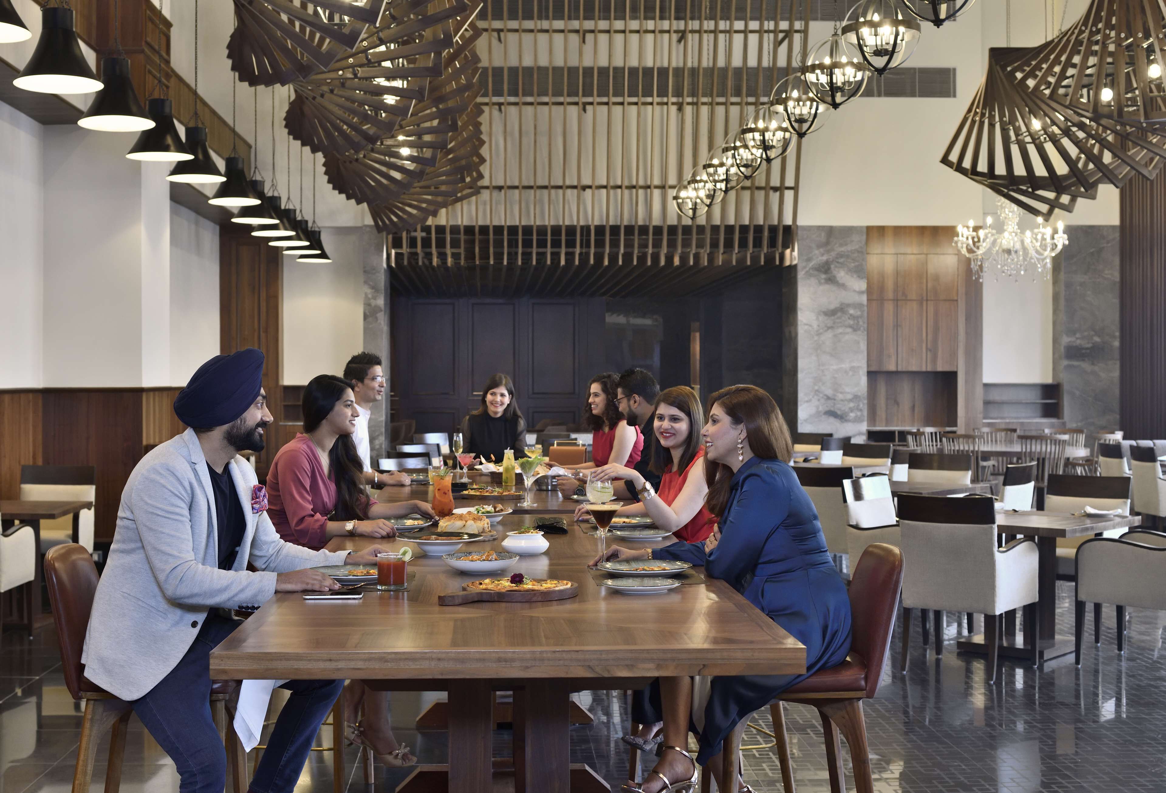 Un grupo de personas cenando en una larga mesa de madera en un restaurante moderno con lámparas colgantes y candelabros.