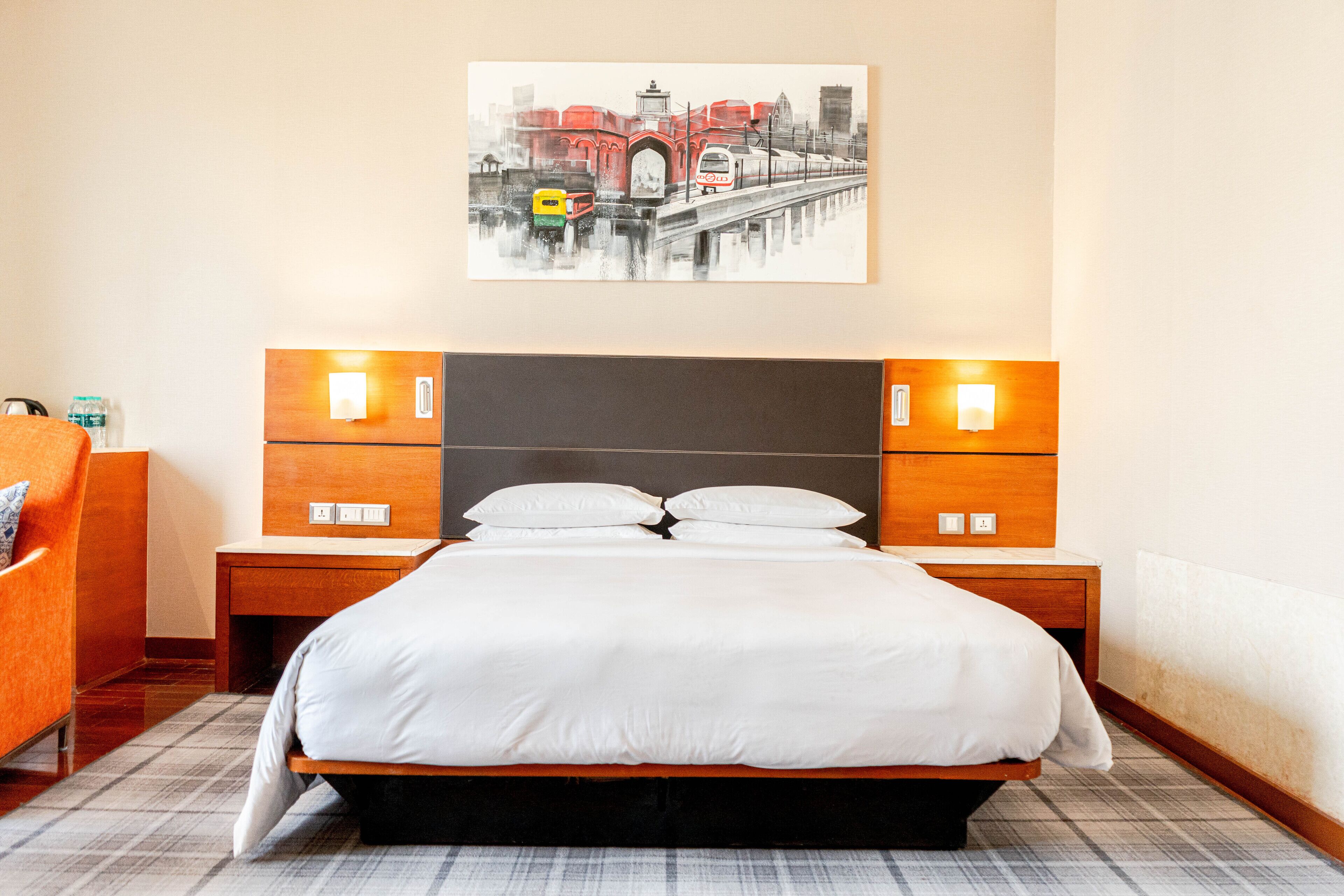 A hotel room with a large bed, two bedside tables, a nightstand, a chair, and a wall-mounted artwork of a bridge.