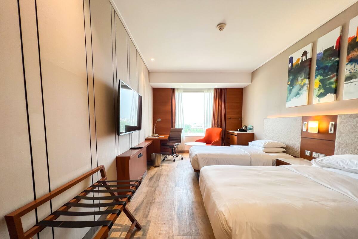 Une chambre d’hôtel avec deux lits, un bureau, une télévision et des œuvres d’art accrochées au mur.