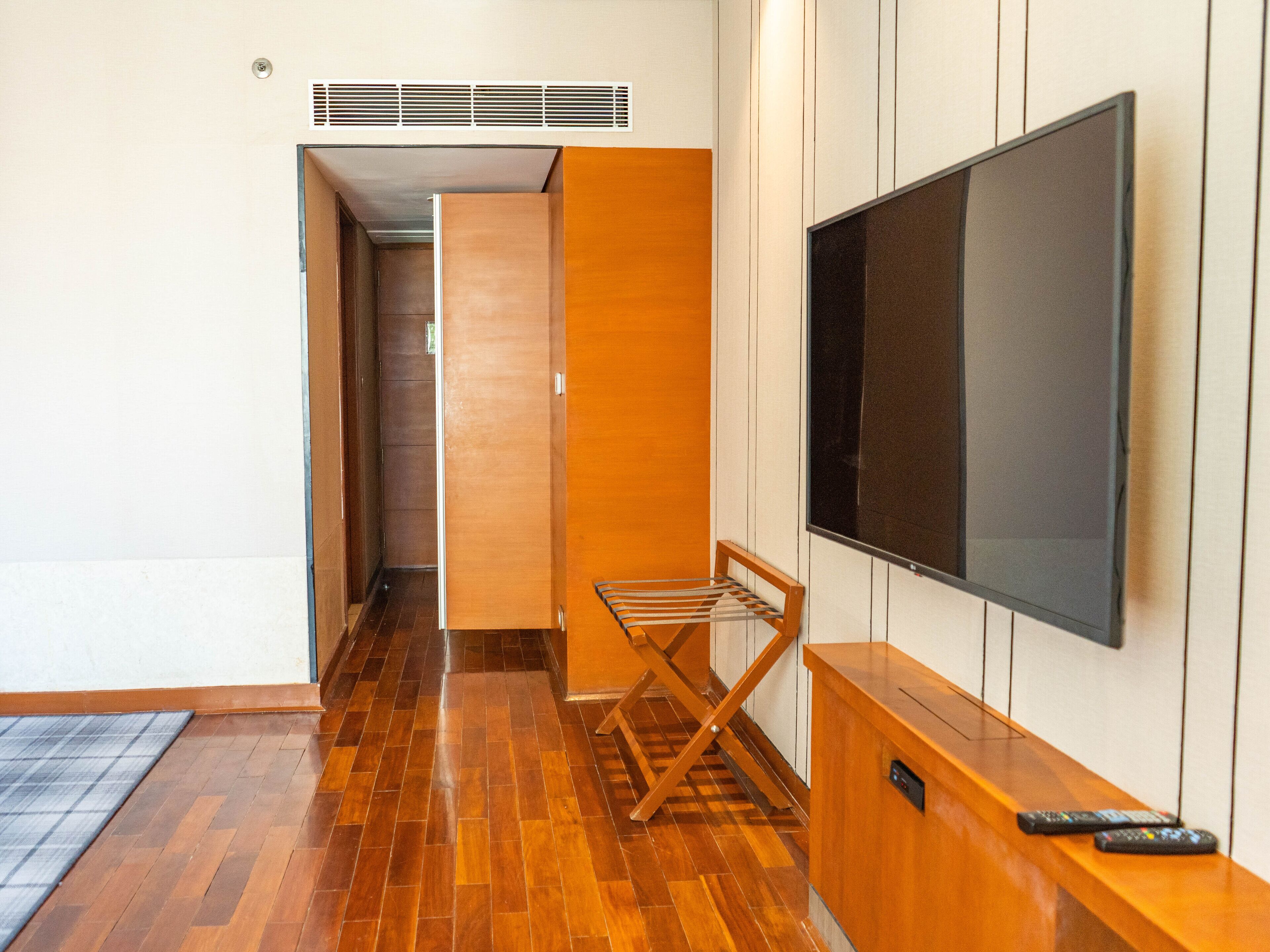A hallway with wooden flooring, a TV mounted on the wall, and a small seating area with a towel rack.