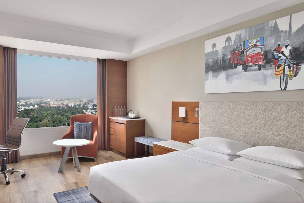 Une chambre d’hôtel avec un grand lit, un bureau, une chaise, une petite table et une vue sur le paysage urbain.