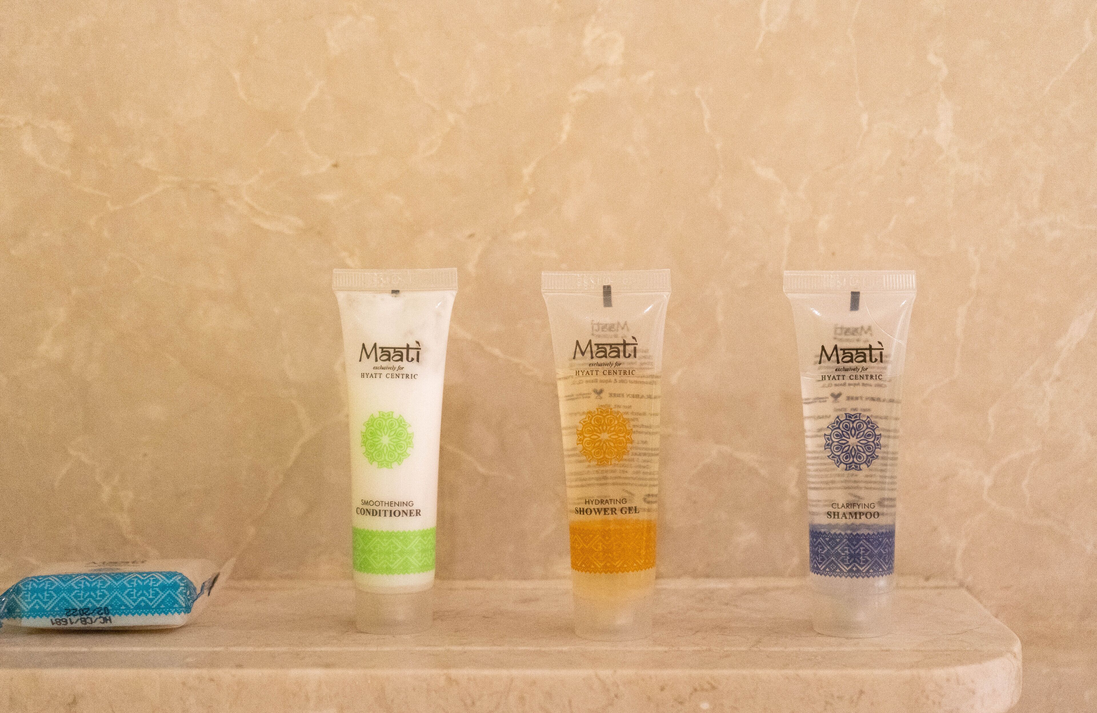 Three Maati hotel-centric products: a moisturizing conditioner, a hydrating shower gel, and a clarifying shampoo, displayed on a marble surface.