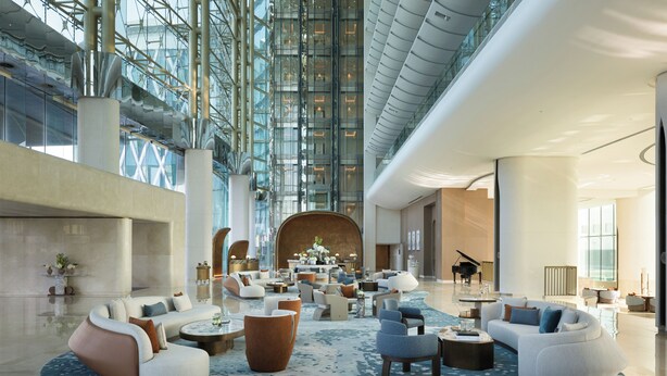 A spacious lobby with modern furniture, a grand piano, and a high ceiling with glass panels. - The Meydan Hotel (Dubai)