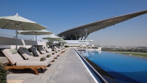 A poolside area with lounge chairs and umbrellas, a clear sky, and a view of the city in the distance. - The Meydan Hotel (Dubai)