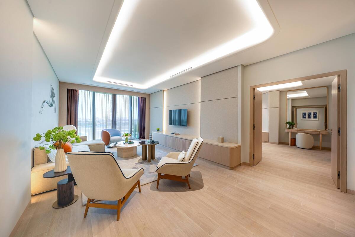 A modern living room with a sofa, two armchairs, a coffee table, and a TV mounted on the wall.