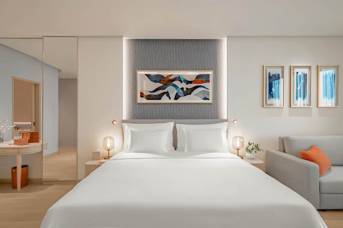 A modern hotel room with a large bed, a desk, and a sofa.