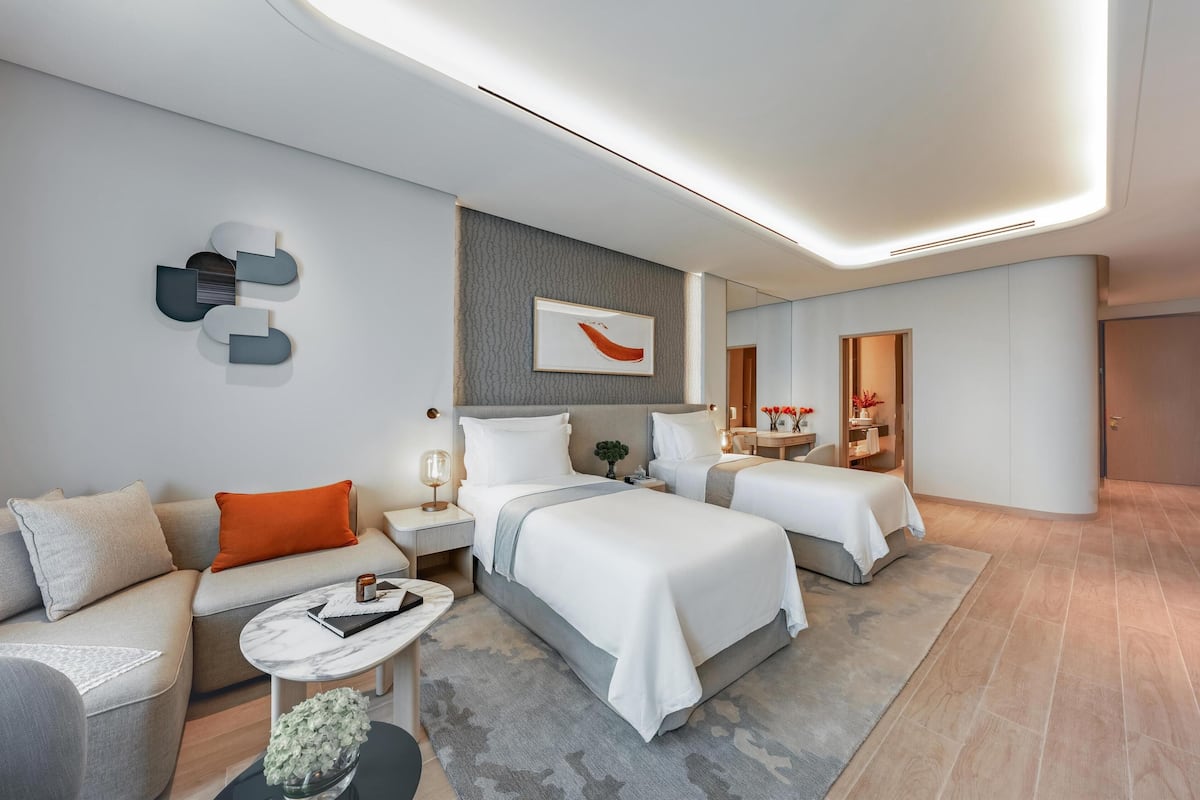 A modern hotel room with two beds, a sofa, a small table, and a mirror.