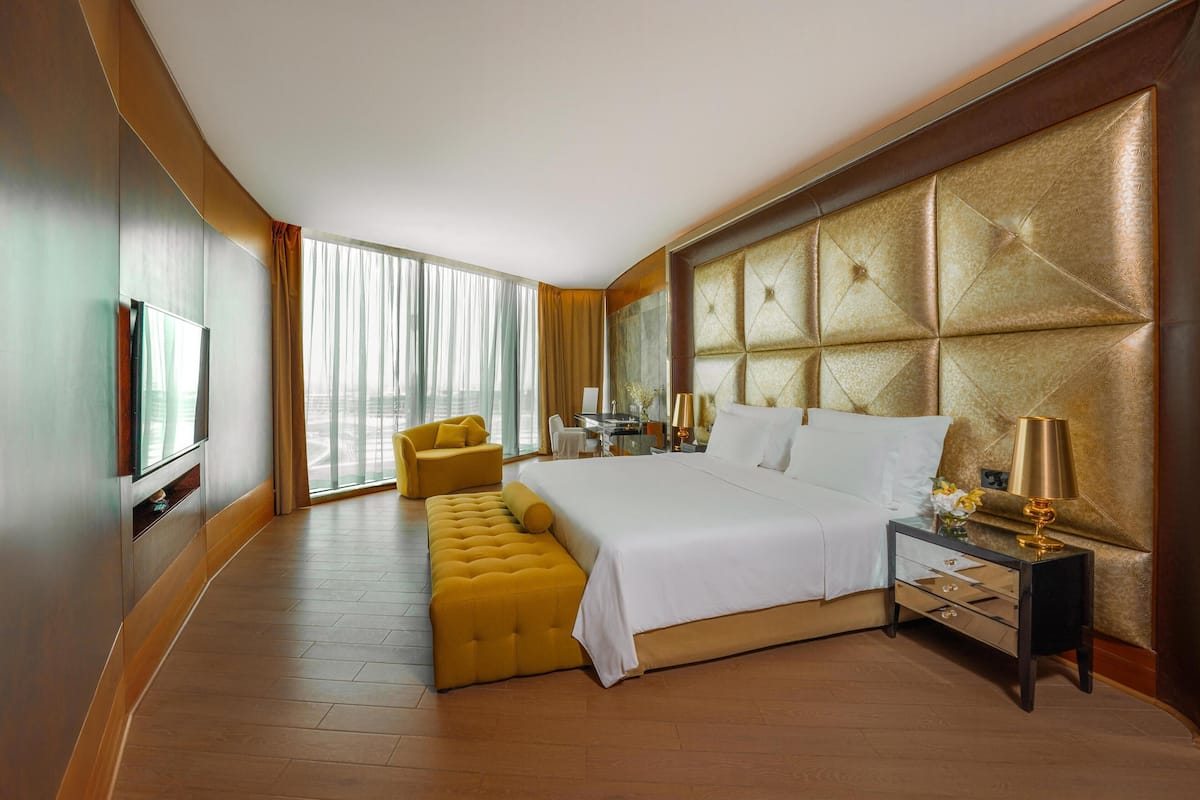 A hotel room with a large bed, a bedside table with a lamp, a small sofa, and a TV.