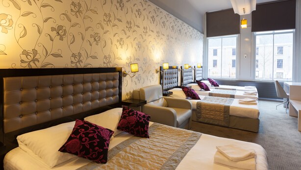 Quarto de hotel com uma cama grande, duas camas menores, um sofá e uma escrivaninha.