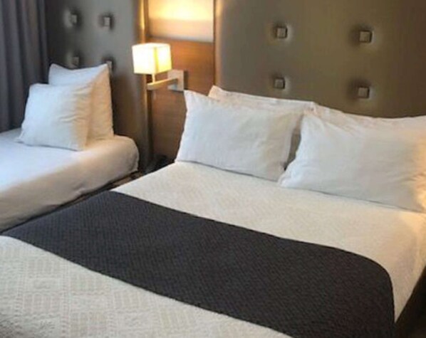 Una habitación de hotel con dos camas, una mesita de noche con lámpara y un cabecero con diseño acolchado.
