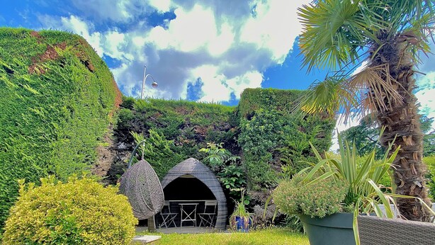 A lush garden with a small, covered structure, possibly a gazebo, surrounded by dense greenery and a palm tree. - Kyriad Lyon Est - Genas Eurexpo (Genas)