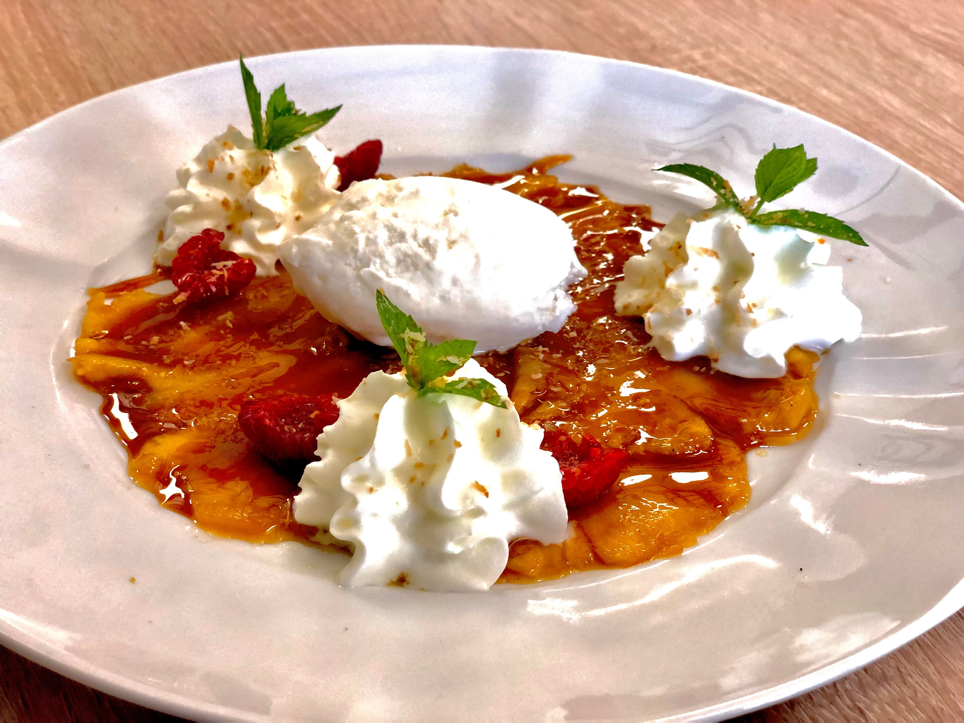 Un plato de postre con cobertura cremosa, trozos de fruta y una ramita de menta.
