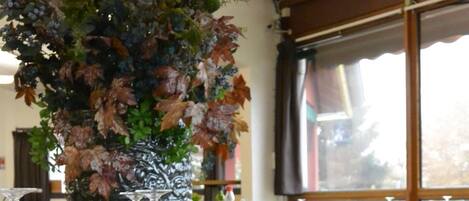 Interior de restaurante con mesas redondas, sillas tapizadas en gris y una pared decorativa con follaje.