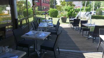 Une terrasse extérieure avec des tables et des chaises, une vue sur un immeuble et une voiture garée.