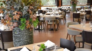 A restaurant with tables set for dining, a decorative plant centerpiece, and a view of the outdoors. - Kyriad Lyon Est - Genas Eurexpo (Genas)