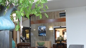 A lobby with a wooden wall, a large vase, a bench, and a chair. - Kyriad Lyon Est - Genas Eurexpo (Genas)