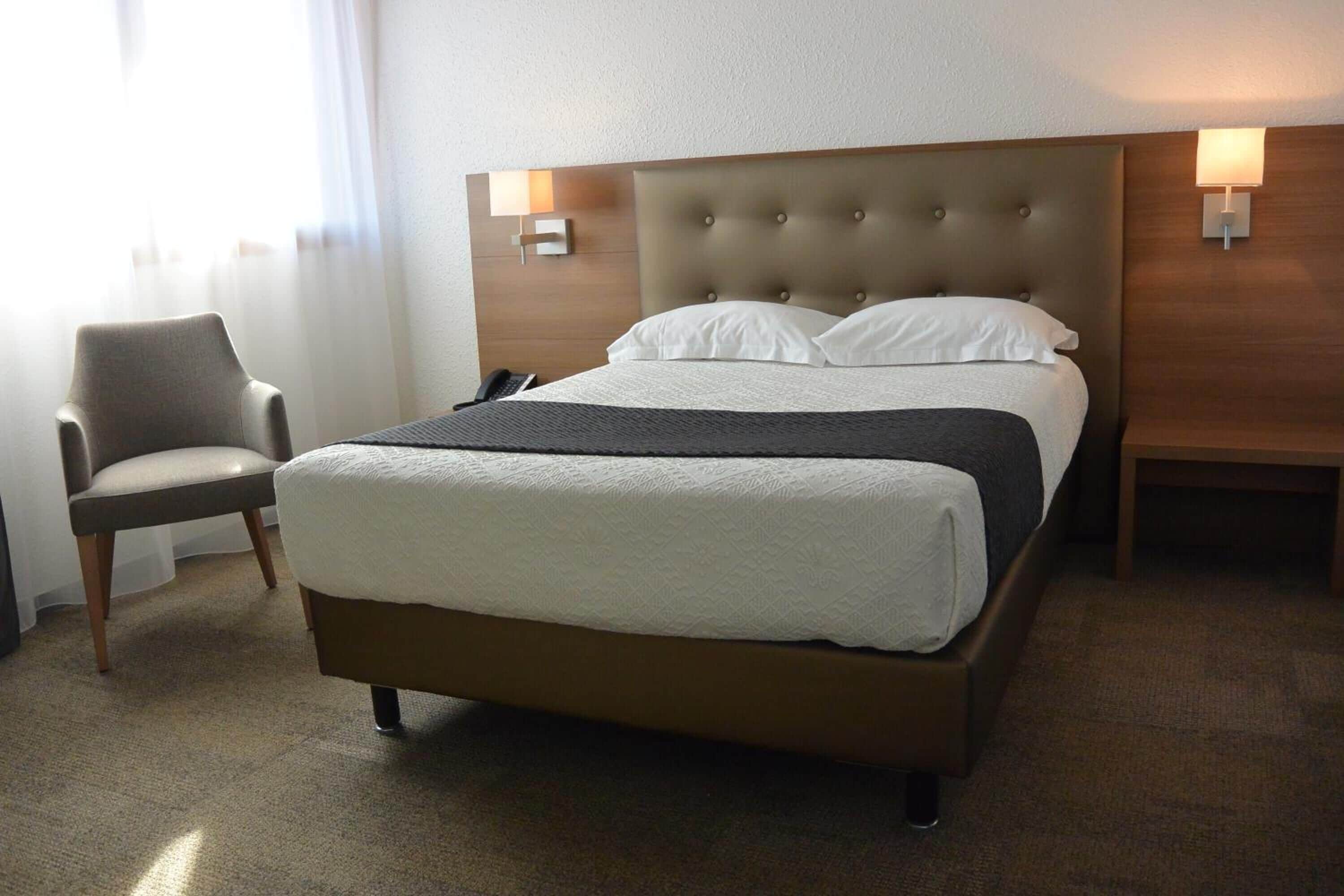 Ett hotellrum med en stor säng, en stol och två sängbord med lampor.